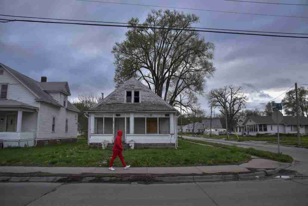 A pedestrian passes in front of a shuttered house in Omaha, Nebraska on a cloudy evening on Thursday, May 3, 2018.